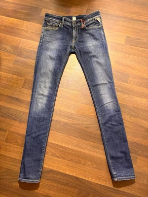 Replay skinny jeans blå denim - Säljer ett par snygga blå skinny jeans från Replay med klassisk femficksdesign, orange detaljer och gul söm. Jeansen har låg midja och är tillverkade i stretchig denim för en tight passform. Märkespatch bak och Replay-logga vid fickan.