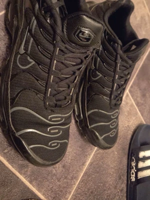 Svarta Nike sneakers med mönster - Säljer ett par svarta Nike sneakers med coola vågformade detaljer i grått på ovandelen. Skorna har snörning, rund tå och är tillverkade i en mix av textil och syntetmaterial. Perfekta för dig som gillar streetwear och sportig stil.