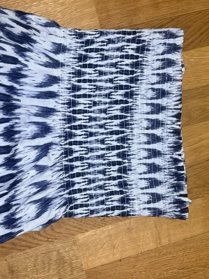 Blåvit  tube topp från Gina Tricot - Säljer en tube  topp från Gina Tricot i blått och vitt med ett coolt abstrakt mönster. Toppen är smockad och axelbandslös, vilket ger en skön och stretchig passform. Perfekt för sommardagar eller festivaler! ( går även att använda som kjol ) storlek 158/164