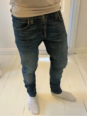 Nudie Jeans Tube Tom blå  - 31W 34L.Säljer ett par Nudie Jeans Tube Tom i mörkblå tvätt med klassiska orangea sömmar och snygga broderade bakfickor. Skinny fit med låg midja och stretchig känsla tack vare bomull och elastan. Perfekt passform för dig som gillar smala jeans.