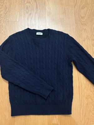 Mörkblå kabelstickad tröja Kappahl - Mörkblå kabelstickad tröja från Kappahl i storlek 146/152. Klassisk rund halsringning och ribbade muddar vid ärmslut och nederkant. 
