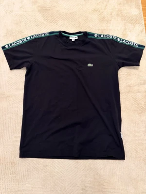 Svart Lacoste t-shirt  - Svart Lacoste T-shirt i nytt skick oanvänd, det står storlek XL men passar främst M/L