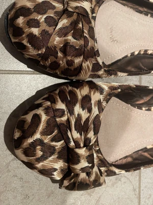 Leopardmönstrade ballerinaskor med rosett - Snygga ballerinaskor med leopardmönster i bruna och beige toner. Skorna har en stor rosett framtill och rund tå. Materialet har en lätt glansig finish som ger extra attityd till outfiten. Perfekta för dig som vill sticka ut lite extra. Passar mig som har storlek 39/40. De har lite sprickor i sulan men inget som påverkar skon eller syns, men därav ett lägre pris.🫶🫶