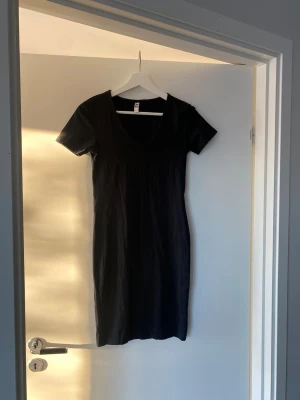 Svart kortklänning från JDY - Enkel och stilren svart kortklänning från JDY i mjuk bomull. Klänningen har korta ärmar och en djup rundringning framtill. Perfekt basplagg att styla med sneakers eller boots.