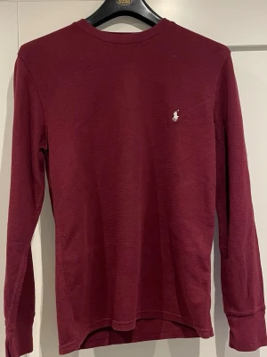 Vinröd långärmad tröja Polo Ralph Lauren - Säljer en vinröd långärmad tröja från Polo Ralph Lauren i storlek M. Toppen har rund halsringning, diskret ribbad struktur och den klassiska broderade loggan i vitt på bröstet. Tillverkad i mjuk bomull som känns skön mot huden.