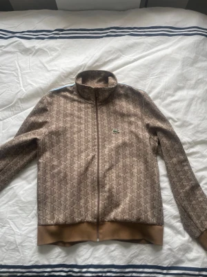 Beige ziptröja Lacoste  - Säljer en beige ziptröja från Lacoste i storlek L men som passar M. Regular fit. Jag har knappt använt den då det inte är min stil därför är den i princip helt ny. Nypris: 2000 Mitt pris: 1050