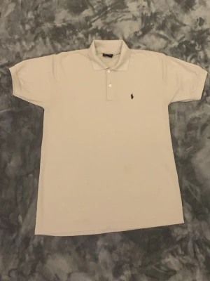 beige Polo Sport pikétröja XL - Klassisk beige pikétröja från Polo Sport i 100% catton. Tröjan har korta ärmar, krage och knäppning med två knappar framtill. Liten broderad logga på bröstet ger en clean och sportig vibe.