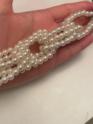 Pärlcollier med kedja halsband - Säljer ett statement-halsband med stora vita pärlor i flera rader, sammanflätade i ett coolt mönster. Halsbandet har en grov silverfärgad kedja som kontrast till pärlorna. Perfekt accessoar för att lyfta vilken outfit som helst.