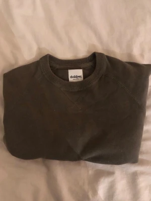 Grön sweatshirt från Dobber - En enkel och stilren grön sweatshirt från Dobber i storlek medium. Tröjan har rund halsringning med ribbade muddar och är tillverkad i mjuk bomull. Perfekt för chill dagar eller när du vill ha en clean look.