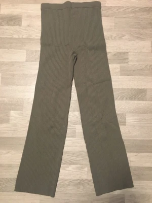 Ribbstickade gröna byxor från H&M - Snygga ribbade byxor i en dämpad grön färg från H&M. Byxorna är högmidjade med raka ben och har en mjuk, stretchig känsla. Perfekta för en chill och trendig look. Materialet är ribbat och ger en extra touch till outfiten.