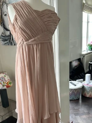Ljusrosa omlottklänning oneshoulder - Säljer en elegant ljusrosa långklänning med omlott-design och oneshoulder. Klänningen har vackra draperade detaljer upptill och ett luftigt, böljande tyg som ger en romantisk känsla. Perfekt för speciella tillfällen och sommarens fester.