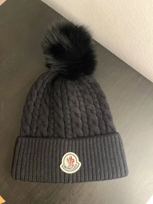 Moncler mössa - Säljer denna svarta Moncler mössa. Mössan är onesize men är lite liten i storleken. Den är i jättebra skick. Kom med bud! Kan gå ner i pris vid snabb affär.