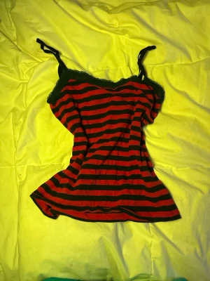 Randig röd och svart linnetopp från Ecue - Säljer en snygg linnetopp från cue i storlek S. Toppen har röda och svarta ränder, tunna axelband och svart spets längs halsringningen. 