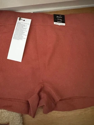 Boxer seamless Lindex  - Rostbrun boxer i sömlös design. Västen har ribbad struktur och är tillverkad i ett mjukt syntetmaterial som sitter skönt mot kroppen. Passformen är normal och färgen är varm och jordnära, perfekt för dig som gillar stilrena basplagg.