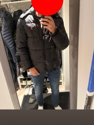 Svart pufferjacka från Polo Ralph Lauren - Svart pufferjacka från Polo Ralph Lauren med röd broderad logga på bröstet. Jackan har huva, flera dragkedjefickor och quiltad design. Materialet är polyester och jackan är långärmad med normal passform. Perfekt för kalla dagar. Och i riktigt bra skick.