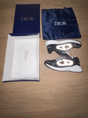 Dior b30 - Säljer ett par svarta Dior sneakers med vita och reflekterande detaljer. Skorna har tjock vit sula, vita snören och tydlig Dior-logga på sidan. Materialet är en mix av textil och syntet. Kommer med originalkartong och dustbag.
