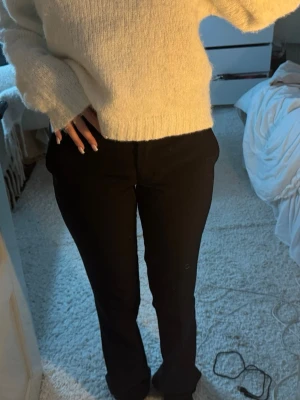 Svarta kostymbyxor med bootcut - Säljer ett par svarta kostymbyxor med bootcut-snitt. Byxorna har en klassisk midja och sitter snyggt över höfterna. Materialet känns mjukt och har en lätt stretch, perfekt för dig som vill ha en clean och stilren look. Passar dig som gillar enkel och tidlös stil.