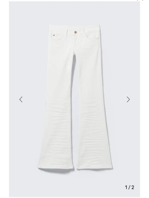 Vita bootcut jeans - Säljer ett par vita bootcut jeans med klassisk femficksdesign och knappgylf. Byxorna har utsvängda ben och är tillverkade i ett mjukt bomullsmaterial som ger en snygg siluett. Perfekta att styla med sneakers eller boots.