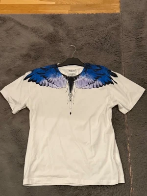 Vit t-shirt med blått vingtryck Marcelo Burlon - En riktigt schysst Marcelo burlon tisha i en unik färg! Tishan är i helt nytt skick! Perfekt plagg för dig som gillar att sticka ut! Hör av dig vid frågor och funderingar. Priset kan diskuteras! 