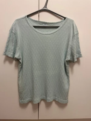 Ljusgrön ribbad topp i 100% bomull strl 50/52 - Ljusgrön ribbad topp i 100% bomull med korta ärmar och rund hals. Toppen har fläckar (se bild). Storlek 50/52.