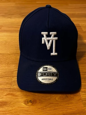 New era up o ner LA mössa - Bilderna visar en mörkblå keps från New Era, modell 9FORTY, med justerbar passform och vit broderad logga framtill. Ingen väst syns på bilderna.
