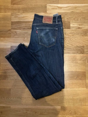 Levi's 511  - Snygga Levi's 511 jeans i mörkblå tvätt med klassisk femficksdesign och smal passform. Jeansen har en diskret slitning och är gjorda i slitstarkt bomullsmaterial med lite stretch för extra komfort. Perfekt för dig som gillar en modern och stilren look.