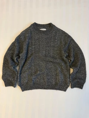 Grå stickad tröja från Zara - Säljer en mörkgrå stickad tröja från Zara med grov struktur och ribbade muddar vid hals, ärmslut och nederkant. Tröjan har en klassisk rund hals och långärmade, loose passform som ger en chill vibe. Perfekt för kyliga dagar.