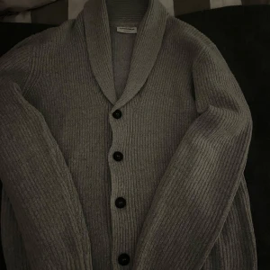 Kofta - Säljer en stilren grå kofta från Lindbergh i storlek S. Koftan har en avslappnad passform med ribbade detaljer och knappar framtill. Perfekt för kyligare dagar.
