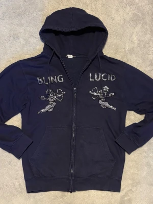 Bling lucid hoodie - En mörkblå Hoodie ifrån bling lucid med rhinestones på framsidan. Tröjorna säljs inte längre vi hemsidan.
