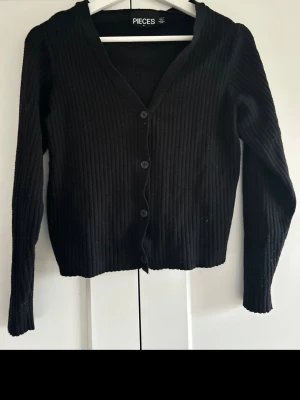 Kofta - Svart kofta från Pieces med ribbad struktur och v-ringad hals.