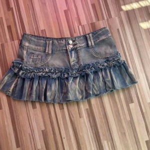Low waist  jeanskjol  - Supersnygg kort jeanskjol i blå denim med slitna detaljer och volangkant. Kjolen har dubbla silverfärgade knappar framtill, klassiska fickor och hällor för bälte. Aldrig använt lånade bilder säg till om du behöver fler. Storlek S