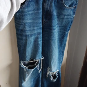 Blå ripped jeans från Zara, strl 36 - Säljer ett par blå jeans från Zara i storlek 36 med snygga slitningar och stora hål vid knäna. Klassisk femficksmodell med raka ben och normal passform. Perfekta för dig som gillar en avslappnad och trendig look.