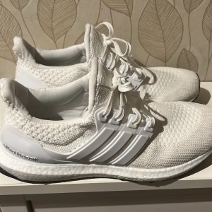 Vita Adidas Ultraboost sneakers - Säljer ett par fräscha Adidas Ultraboost sneakers i helvitt. Skorna har stickad ovandel, klassiska tre ränder på sidan och snörning. Boost-sulan ger grym komfort och respons. Perfekta för dig som gillar stilrena och sportiga sneakers.