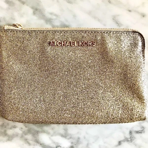 Glittrig guld kuvertväska Michael Kors - Snygg kuvertväska från Michael Kors med glittrig guldframsida och mörkbrun baksida med MK-mönster. Väskan har två separata fack med dragkedja och en guldfärgad handledsrem. Perfekt för att hålla koll på dina essentials och addera lite extra bling till din look.