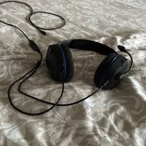 Kabelanslutet spelheadset med mikrofon - Bekvämt kabelanslutet spelheadset med justerbar mikrofon och mjuka öronkuddar. Passar perfekt för gaming och samtal. 3,5 mm kontakt för bred kompatibilitet. Svart design med blå detaljer. Ser ut att vara i gott skick utan synligt slitage.