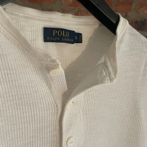 Vit långärmad tröja Polo Ralph Lauren - Vit långärmad tröja från Polo Ralph Lauren i storlek S. Tröjan har en ribbad struktur, rund hals och tre knappar framtill. Perfekt för chill dagar och har en clean, klassisk look som funkar till allt. Materialet är mjukt och känns skönt mot huden.