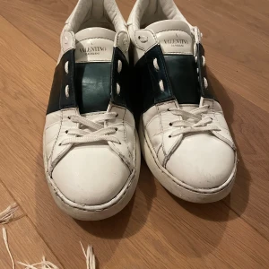 Valentino Garavani sneakers vit/grön - Snygga sneakers från Valentino Garavani i vitt skinn med bred mörkgrön läderdetalj över snörningen. Köpt för 3640 DKK. Inte har box!!