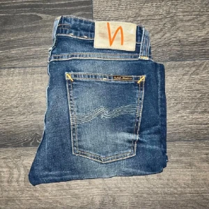 Nudie Jeans - Säljer ett par blå skinny jeans från märket Nudie Jeans med den klassiska orangea sömmen och den vågiga brodyren på bakfickorna. Jeansen har hög midja och är gjorda i stretchig bomull som ger en tight passform. Snygga slitningar både framtill och baktill. Modell: Skinny Lin. Längd 96 cm. Om det inte finns någon bild i annonsen där jag har på mig plagget beror det på att jag inte kan ha storleken eller passformen, så kolla gärna måtten för storlek och sök på modellnamnet 😉