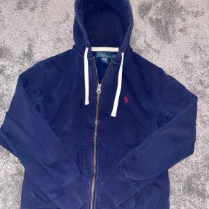 Marinblå Zip-up hoodie från Polo Ralph Lauren från 90-talet - Säljer en vintage marinblå Zip-up hoodie från Polo Ralph Lauren då den har blivit för liten. Den passar XS och S. Har inga tecken på användning och säljer den för premium pris då den annars kostar 822kr begagnat på nätet (se sista bilden). Skriv för fler bilder.