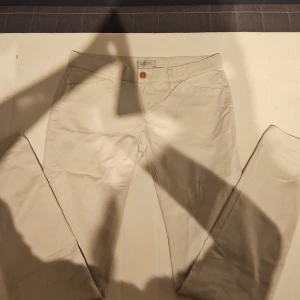 Beiga chinos från Hunkydory Essentials - Snygga beiga chinos från Hunkydory Essentials med klassisk passform. Byxorna har raka ben, framfickor och bakfickor samt stängs med en brun knapp. Tillverkade i bomull för en skön känsla och stilren look. Strl är W28 och L32