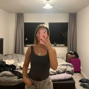 Mörkgrått linne - Säljer en stilren mörkgrå linnetopp med breda axelband och rundad halsringning. Perfekt att matcha med jeans eller kjol för en enkel och snygg look. Materialet känns mjukt och följsamt mot kroppen.