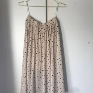 Beige långkjol med svarta prickar - Säljer en beige långkjol med svarta prickar. Kjolen har en luftig och flowy passform med resår i midjan för extra komfort. Perfekt för dig som gillar retrovibbar och vill sticka ut med ett lekfullt mönster. Passar till sneakers eller boots