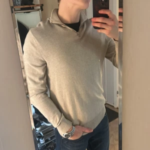 Beige half zip tröja Jack & Jones - Snygg beige långärmad tröja från Jack & Jones med half zip och krage. Tröjan är i mjuk bomull och har en clean, normal passform som funkar till jeans eller chinos. Perfekt för dig som gillar stilrena och enkla plagg med lite edge. Passar utmärkt med en skjorta under och tröjan är i helt nyskick, skriv gärna om du har några frågor