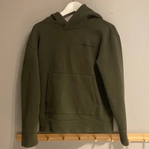 Mörkgrön hoodie från Sail Racing - Snygg mörkgrön hoodie från Sail Racing med diskret logga på bröstet. Tröjan har huva, stor magficka och långa ärmar. Materialet är mjuk bomull med en skön känsla. Perfekt för chill dagar och enkel att matcha med jeans eller joggers.
