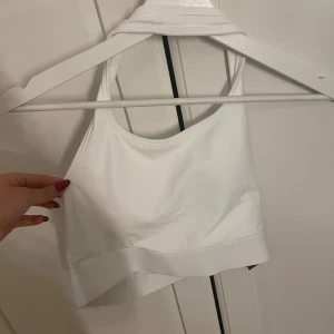 Vit croppad linnetopp från nova sports - Säljer en vit croppad linnetopp från  Nova sports med breda axelband och rundad halsringning. Toppen är öppen i ryggen och har en stilren, enkel design i mjukt och stretchigt syntetmaterial. Perfekt för att styla med jeans eller shorts. Köppt för ca 400kr