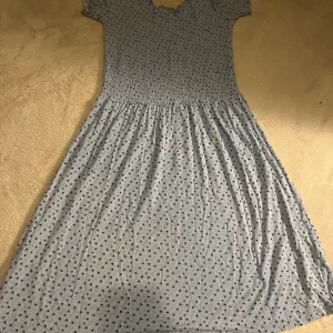 Ljusblå blommig långklänning Stories - Supersöt ljusblå långklänning från Stories i storlek S, med små svarta blommor över hela tyget. Klänningen har korta ärmar, smock upptill och en flowy kjol. Perfekt för dig som gillar romantisk och chill stil.