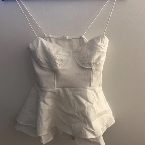 Vit korsett-topp från Zara - Supersöt vit korsett-topp från Zara med tunna axelband och volangig peplum-nederdel. Toppen har markerade kupor och dragkedja i sidan. Perfekt för sommarens alla tillfällen när du vill känna dig extra fin.
