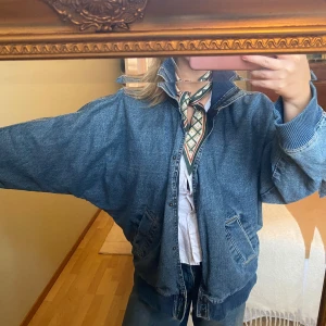 Oversized jeansjacka från Zara - Säljer en oversized blå jeansjacka från Zara med bred ribbad krage och muddar. Jackan har dragkedja och knappar framtill samt två snedställda fickor. Perfekt för dig som gillar en loose och avslappnad stil.