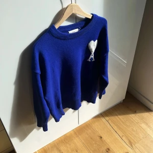 Blå stickad tröja från Ami Paris - Säljer en blå stickad tröja från Ami Paris med rund hals och ribbade muddar. På bröstet finns Ami:s ikoniska vita hjärta med A. Tröjan har en loose passform och är perfekt för dig som gillar stilren design med en twist. Strl ~ S| Utmärkt skick 10/10. Förbrukad 1 enda gång🙌🏽 Tags - påse medföljs👍🏽 Mvh ItsForfits