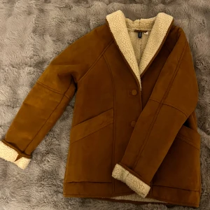 Brun teddyjacka från H&M Divided - Säljer en brun teddyjacka från H&M Divided i storlek S. Jackan har mjukt, vitt teddyfoder, stora knappar framtill och bred krage. Utsidan är i mockaliknande material och insidan är fluffig och varm.
